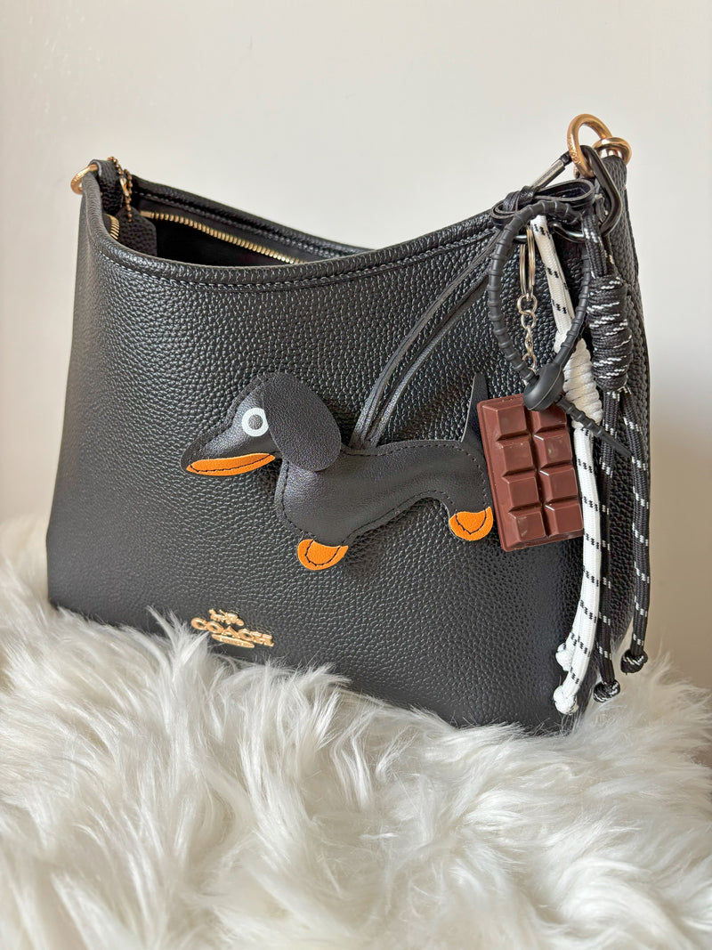 Gray handbag with Dapper Dachshund Keychain and chocolate bar charm on a white fur surface