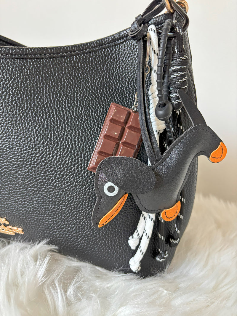 Black textured handbag with Dog-shaped Dapper Dachshund keychain and chocolate bar charm on a white fur background