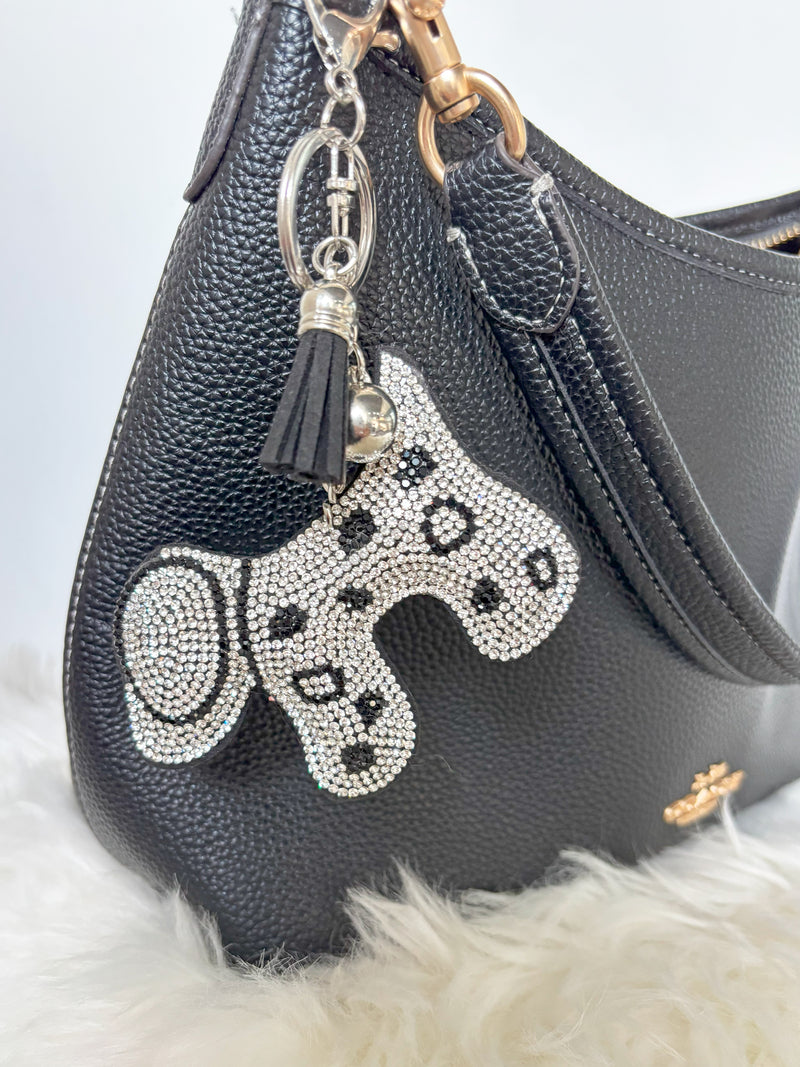 Black handbag with Zelci's Glam Dalmatian Keychain featuring paw prints on a light gray background