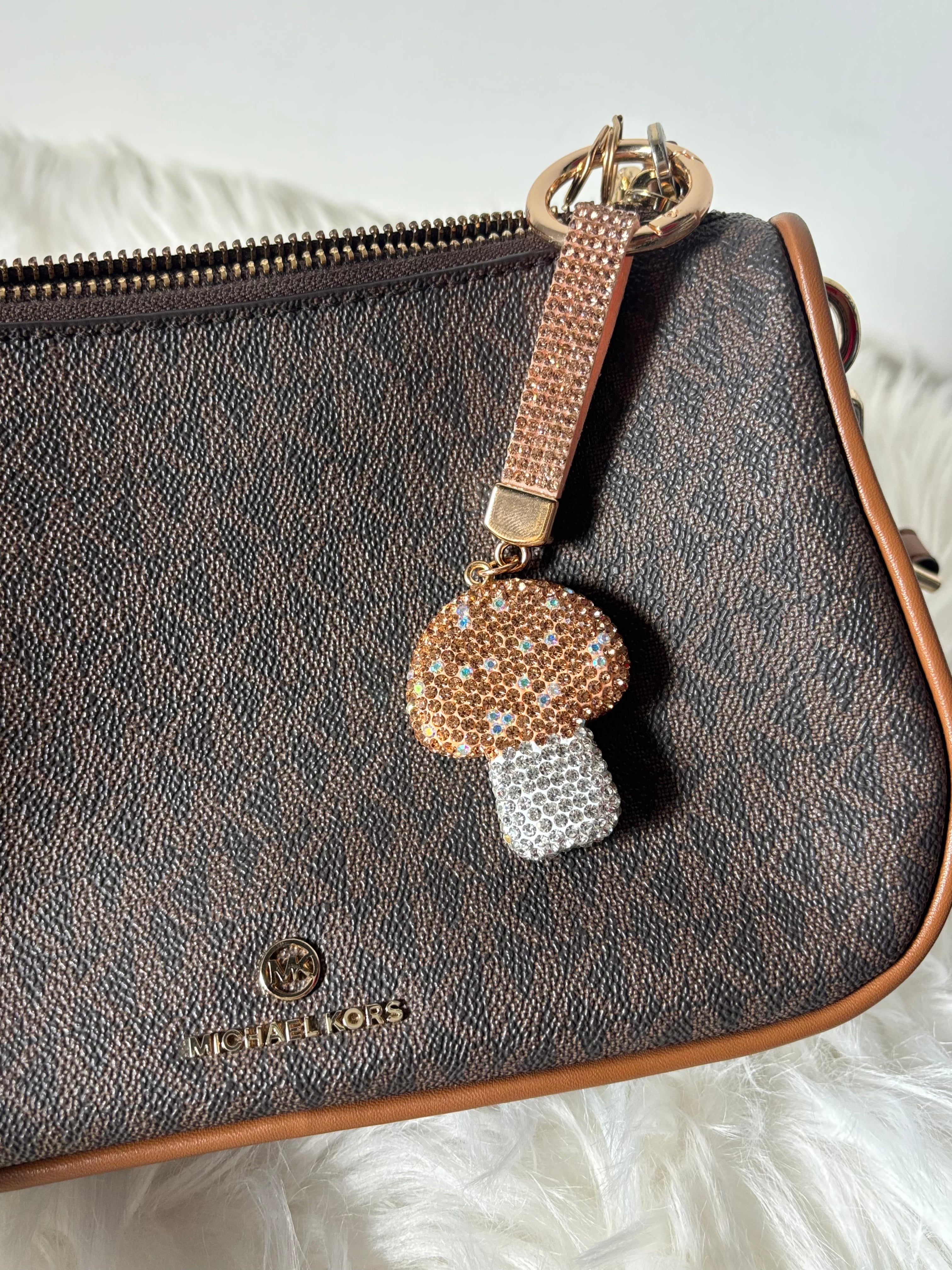 Brown leather handbag with a decorative mushroom keychain on a white surface